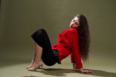 Kırmızı ceketli şehvetli bir genç kadın, külotlu ve uzun siyah saçlı ayakkabılar stüdyoda yeşil bir arka planda poz veriyor..