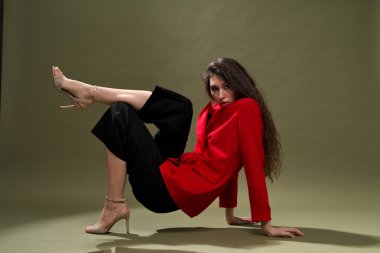 Kırmızı ceketli şehvetli bir genç kadın, külotlu ve uzun siyah saçlı ayakkabılar stüdyoda yeşil bir arka planda poz veriyor..