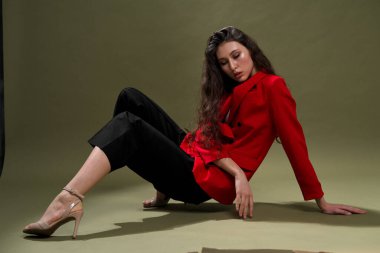 Kırmızı ceketli şehvetli bir genç kadın, külotlu ve uzun siyah saçlı ayakkabılar stüdyoda yeşil bir arka planda poz veriyor..