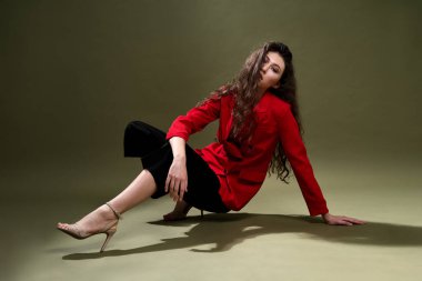 Kırmızı ceketli şehvetli bir genç kadın, külotlu ve uzun siyah saçlı ayakkabılar stüdyoda yeşil bir arka planda poz veriyor..