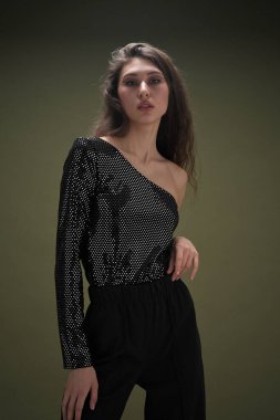 Uzun siyah saçlı, uzun boylu güzel bir kız parlak bir bluz ve yeşil arka planda siyah külotlar giyiyor. Buty ve moda fotoğraf çekimi.