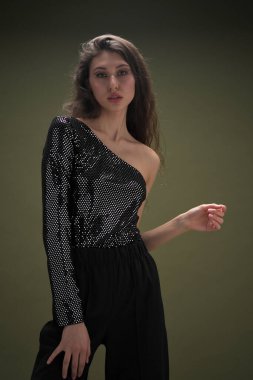 Uzun siyah saçlı, uzun boylu güzel bir kız parlak bir bluz ve yeşil arka planda siyah külotlar giyiyor. Buty ve moda fotoğraf çekimi.