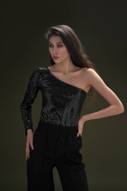 Uzun siyah saçlı, uzun boylu güzel bir kız parlak bir bluz ve yeşil arka planda siyah külotlar giyiyor. Buty ve moda fotoğraf çekimi.