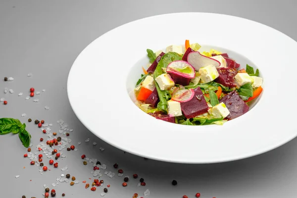 Овочевий салат з редькою, м'яким сиром, буряком і зеленню в білій тарілці на сірому фоні. Закуски в ресторані . — стокове фото