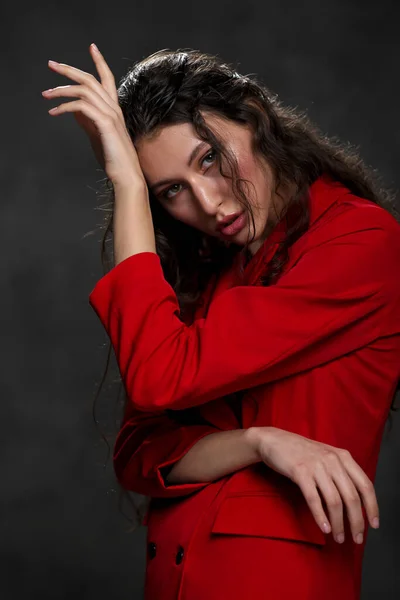 Una giovane bella donna orientale con lunghi capelli neri in una giacca rossa su uno sfondo nero. La modella posa in studio. — Foto Stock