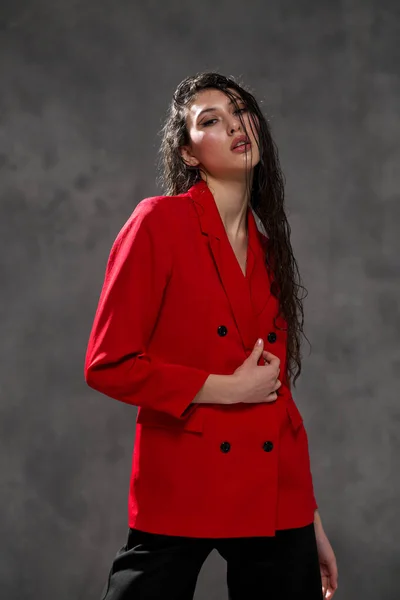 Una giovane bella donna orientale con lunghi capelli neri in una giacca rossa su uno sfondo nero. La modella posa in studio. — Foto Stock