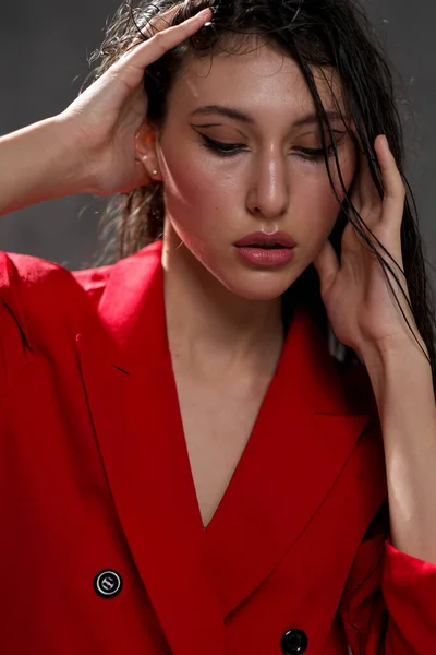 A young beautiful oriental woman with long black hair in a red jacket against a black background. The fashion model poses in the studio. — Stock Photo, Image