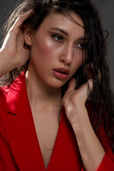 Una joven hermosa mujer oriental con el pelo largo y negro en una chaqueta roja sobre un fondo negro. La modelo posa en el estudio. —  Fotos de Stock