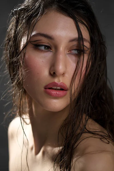 The face of a beautiful young girl with wet black hair close-up. Eastern appearance. Nude makeup, natural skin.