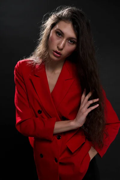 Uma mulher oriental bonita nova com cabelo preto longo em uma jaqueta vermelha contra um fundo preto. O modelo de moda posa no estúdio. — Fotografia de Stock