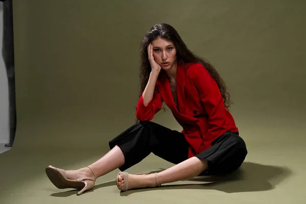 Zmysłowa młoda kobieta w czerwonej kurtce, okularach i butach z mokrymi długimi czarnymi włosami na zielonym tle w studio. — Zdjęcie stockowe