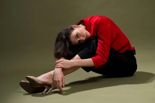 Een sensuele jonge vrouw in een rood jasje, culottes en schoenen met nat lang zwart haar poseert tegen een groene achtergrond in de studio. — Stockfoto