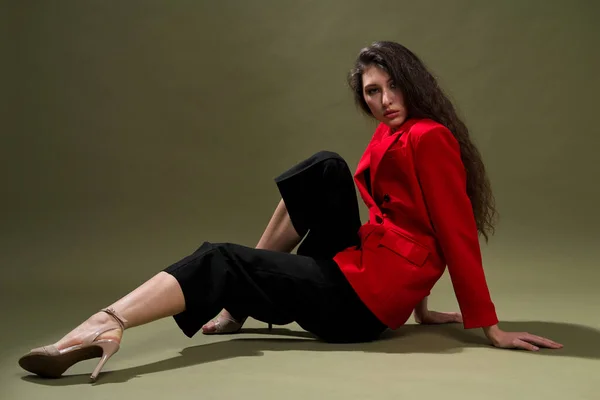 Чуттєва молода жінка в червоній куртці, костюми та взуття з мокрими довгими чорними позуваннями волосся на зеленому тлі в студії . — стокове фото