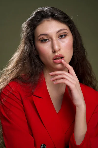 Чуттєва молода жінка портрет в червоній куртці, з мокрим довгим чорним волоссям позує на зеленому тлі в студії . — стокове фото