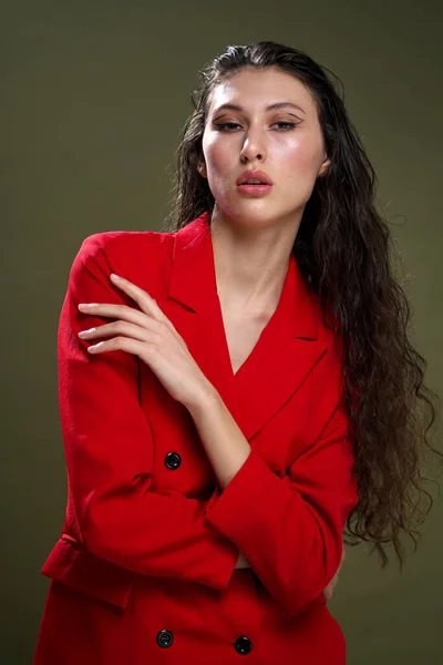 Een sensuele jonge vrouw portret in een rode jas, met nat lang zwart haar poseert tegen een groene achtergrond in de studio. — Stockfoto