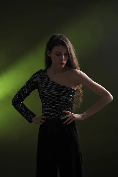 Красива молода дівчина з довгим чорним волоссям позує в блискучій блузці і чорних коктейлях на зеленому тлі. Буті і модна фотосесія . — стокове фото