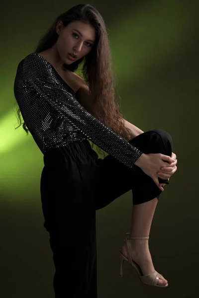 Uma bela menina alta com longos cabelos pretos posa em uma blusa brilhante e seitas pretas em um fundo verde. Buty e moda sessão de fotos. — Fotografia de Stock