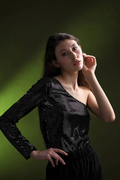 Ein schönes junges Mädchen mit langen schwarzen Haaren posiert in einer glänzenden Bluse und schwarzen Culottes auf grünem Hintergrund. Pflicht und Mode Foto-Shooting. — Stockfoto