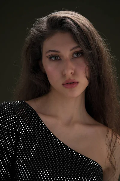 Uma bela menina alta com longos cabelos pretos posa em uma blusa brilhante e seitas pretas em um fundo verde. Buty e moda sessão de fotos. — Fotografia de Stock