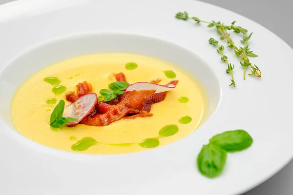 Corn cream soup with smoked meat in a white plate decorated with basil, on a gray background. The first course on the restaurant menu. — Stock Image Corn cream soup with smoked meat in a white plate decorated with basil, on a gray background. The first course on the restaurant menu. Stock Image