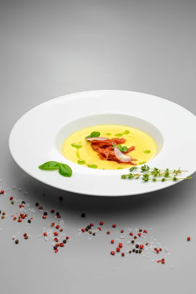 Corn cream soup with smoked meat in a white plate decorated with basil, on a gray background. The first course on the restaurant menu. — Stock Image Corn cream soup with smoked meat in a white plate decorated with basil, on a gray background. The first course on the restaurant menu. Stock Image