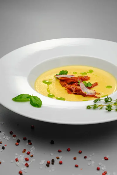 Corn cream soup with smoked meat in a white plate decorated with basil, on a gray background. The first course on the restaurant menu. — Stock Image Corn cream soup with smoked meat in a white plate decorated with basil, on a gray background. The first course on the restaurant menu. Royalty Free Stock Photos