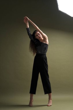 Uzun siyah saçlı, uzun boylu güzel bir kız parlak bir bluz ve yeşil arka planda siyah külotlar giyiyor. Buty ve moda fotoğraf çekimi.