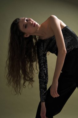 Uzun siyah saçlı, uzun boylu güzel bir kız parlak bir bluz ve yeşil arka planda siyah külotlar giyiyor. Buty ve moda fotoğraf çekimi.