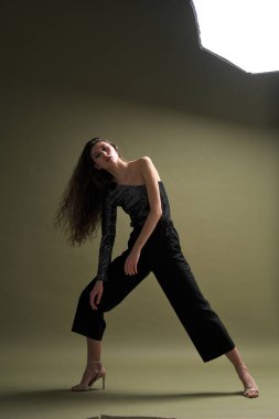 Uzun siyah saçlı, uzun boylu güzel bir kız parlak bir bluz ve yeşil arka planda siyah külotlar giyiyor. Buty ve moda fotoğraf çekimi.