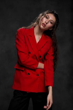 Siyah arka planda, kırmızı ceketli, uzun siyah saçlı, güzel, doğulu bir kadın. Model stüdyoda poz veriyor..
