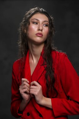 Siyah arka planda, kırmızı ceketli, uzun siyah saçlı, güzel, doğulu bir kadın. Model stüdyoda poz veriyor..