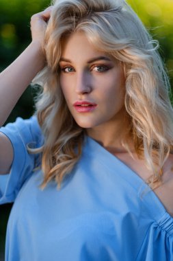 21 yaşında, mavi bir yaz elbisesi içinde beyaz kemer çantalı güzel bir kızın portresi. Kadın gülümsüyor. Güzel dudaklar ve gözler. Uzun gevşek saçlar.