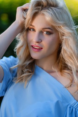 21 yaşında, mavi bir yaz elbisesi içinde beyaz kemer çantalı güzel bir kızın portresi. Kadın gülümsüyor. Güzel dudaklar ve gözler. Uzun gevşek saçlar.