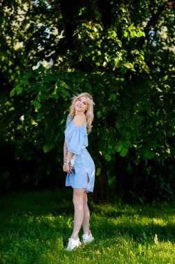 21 yaşında, mavi bir yaz elbisesi içinde beyaz kemer çantalı güzel bir kızın portresi. Kadın gülümsüyor. Güzel dudaklar ve gözler. Uzun gevşek saçlar.