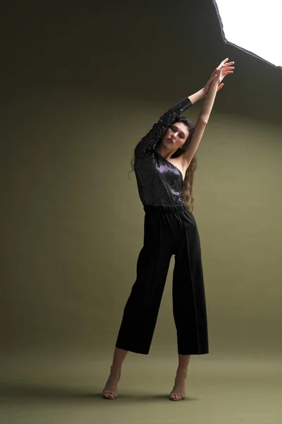 Uma bela menina alta com longos cabelos pretos posa em uma blusa brilhante e seitas pretas em um fundo verde. Buty e moda sessão de fotos. — Fotografia de Stock