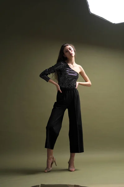 Uma bela menina alta com longos cabelos pretos posa em uma blusa brilhante e seitas pretas em um fundo verde. Buty e moda sessão de fotos. — Fotografia de Stock