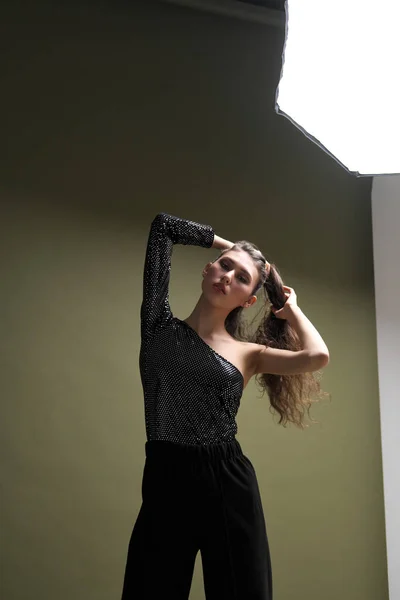 Una hermosa joven alta con el pelo largo y negro posa en una blusa brillante y culottes negros sobre un fondo verde. Buty y sesión de fotos de moda. — Foto de Stock