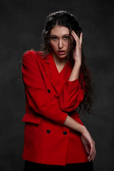 A young beautiful oriental woman with long black hair in a red jacket against a black background. The fashion model poses in the studio. — Stock Photo, Image