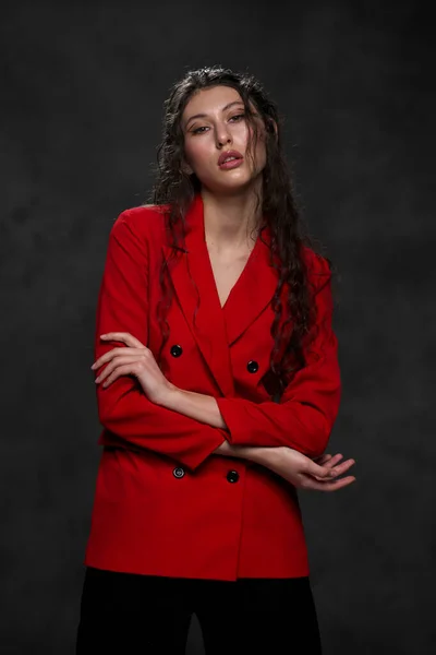 Молода красива східна жінка з довгим чорним волоссям у червоній куртці на чорному тлі. Модна модель позиціонується в студії . — стокове фото