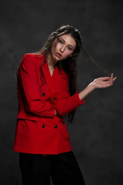 A young beautiful oriental woman with long black hair in a red jacket against a black background. The fashion model poses in the studio. — Stock Photo, Image