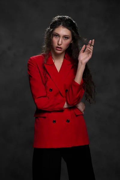 A young beautiful oriental woman with long black hair in a red jacket against a black background. The fashion model poses in the studio.