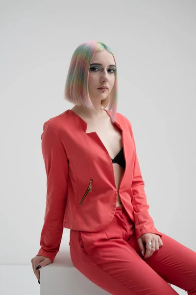 Portrait of a young beautiful informal blonde girl with dyed hair. Red jacket suit on the naked body. Studio photoshoot on a white background.