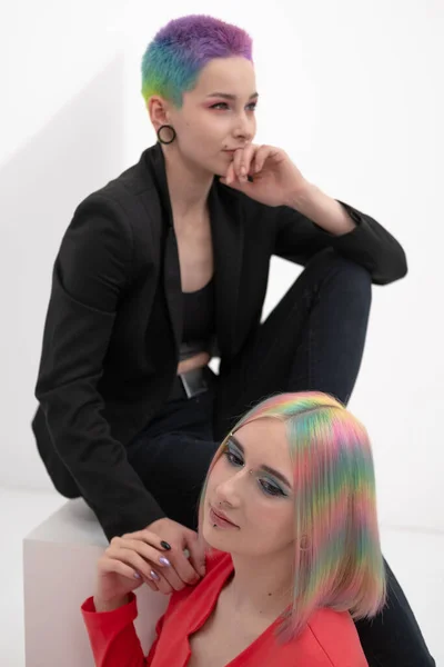 Young lesbian woman couple with vivd colored short hair and jackets posing on white background. Piercing on the face, tunnels in the ears. — Stock Photo, Image
