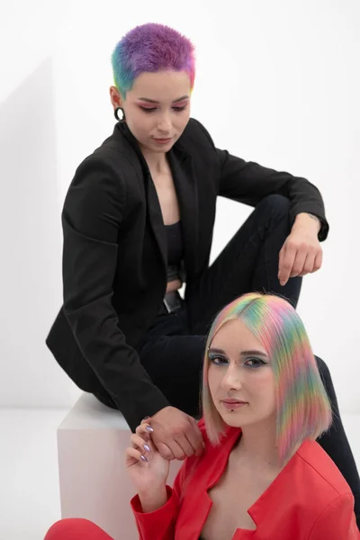 Young lesbian woman couple with vivd colored short hair and jackets posing on white background. Piercing on the face, tunnels in the ears. — Stock Photo, Image