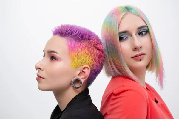 Young lesbian woman couple with vivd colored short hair and jackets posing on white background. Piercing on the face, tunnels in the ears. — Stock Photo, Image