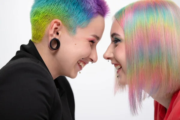 若いレズビアンの女性のカップルは、白い背景にポーズをとった鮮やかな色の短い髪とジャケットを持っています。顔にピアス、耳のトンネル. — ストック写真