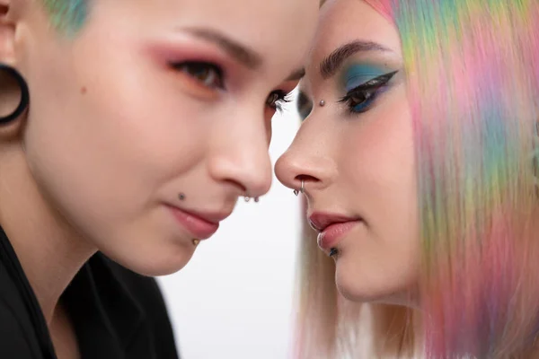 Young lesbian woman couple with vivd colored short hair and jackets posing on white background. Piercing on the face, tunnels in the ears. — Stock Photo, Image