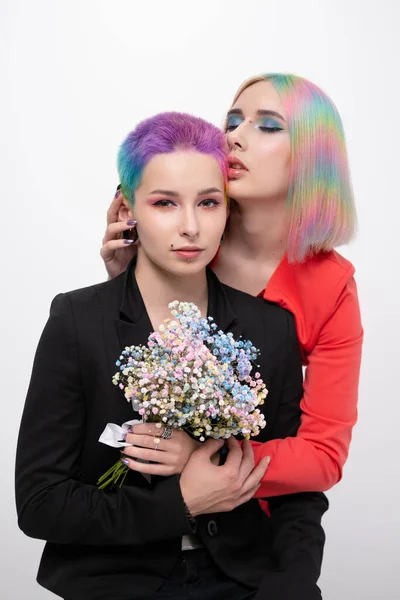 Young lesbian woman couple with vivd colored short hair and jackets posing on white background. Piercing on the face, tunnels in the ears. — Stock Photo, Image