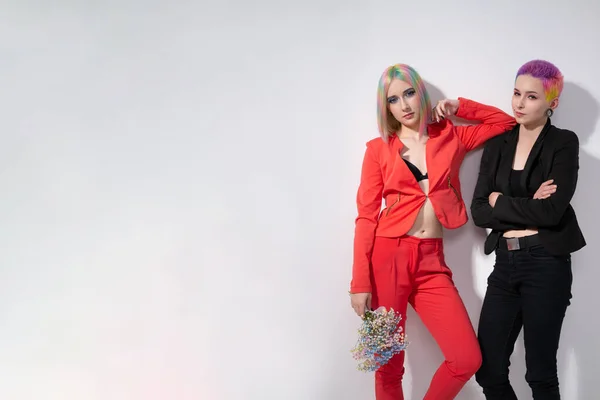 Young lesbian woman couple with vivd colored short hair and jackets posing on white background. Piercing on the face, tunnels in the ears. — Stock Photo, Image