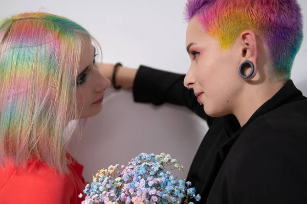 年轻的女同性恋夫妇，有着活泼的彩色短发和白色背景的外套。在脸上穿孔，在耳朵里挖隧道. — 图库照片